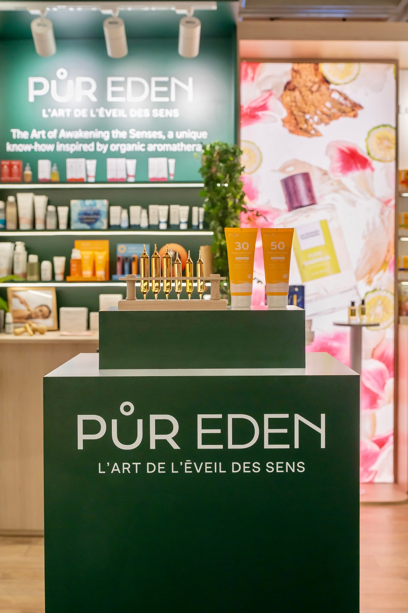 Colonne de présentation verte Pür Eden devant le mur de produits et le caisson lumineux floral